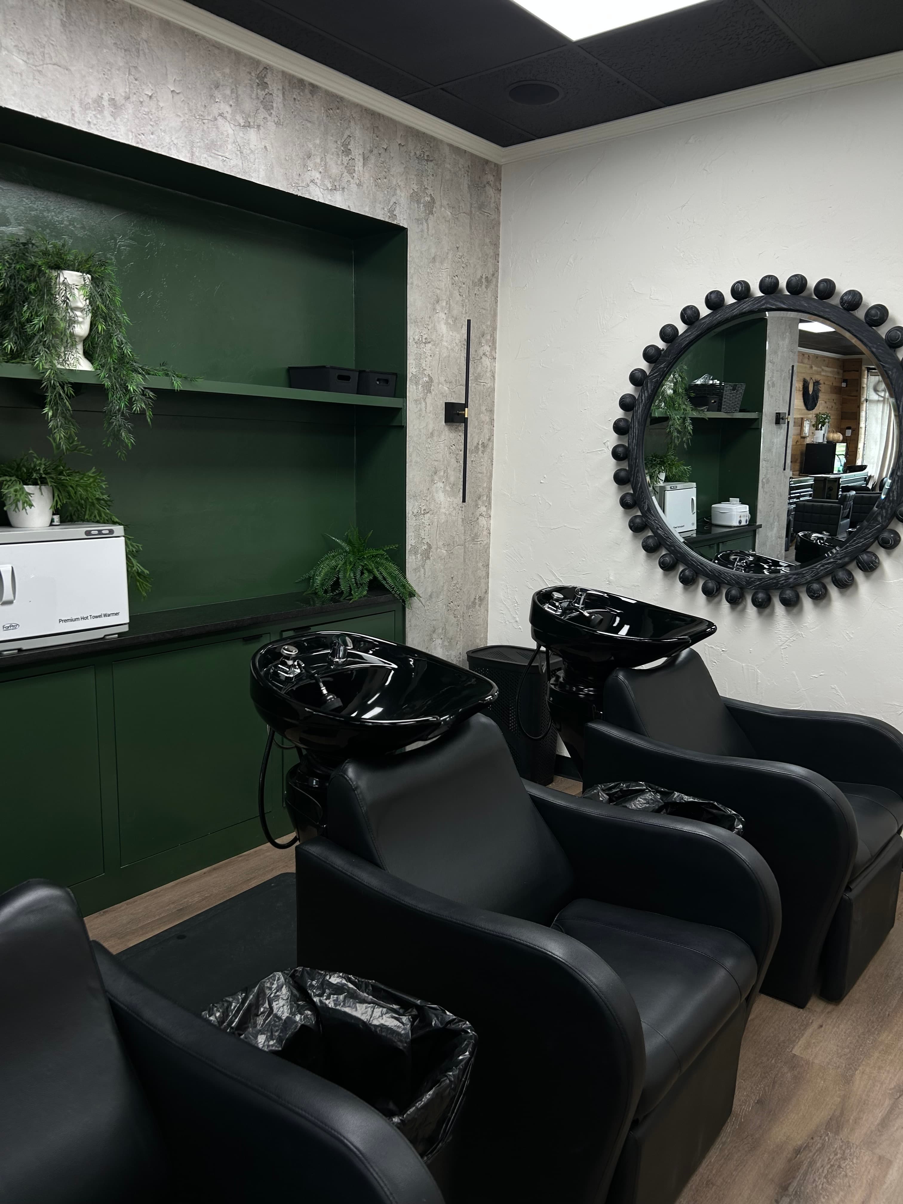 Hair washing stations with black shampoo bowls and modern green decor at The Hair Collective salon in Oklahoma City