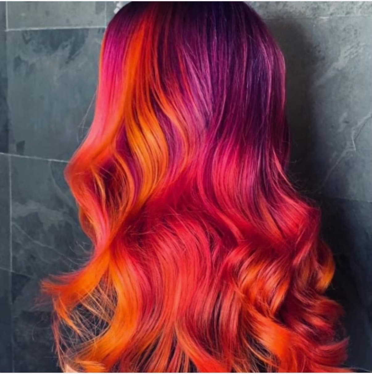 Vibrant red, orange, and magenta creative hair color styled in waves by The Hair Collective Oklahoma City